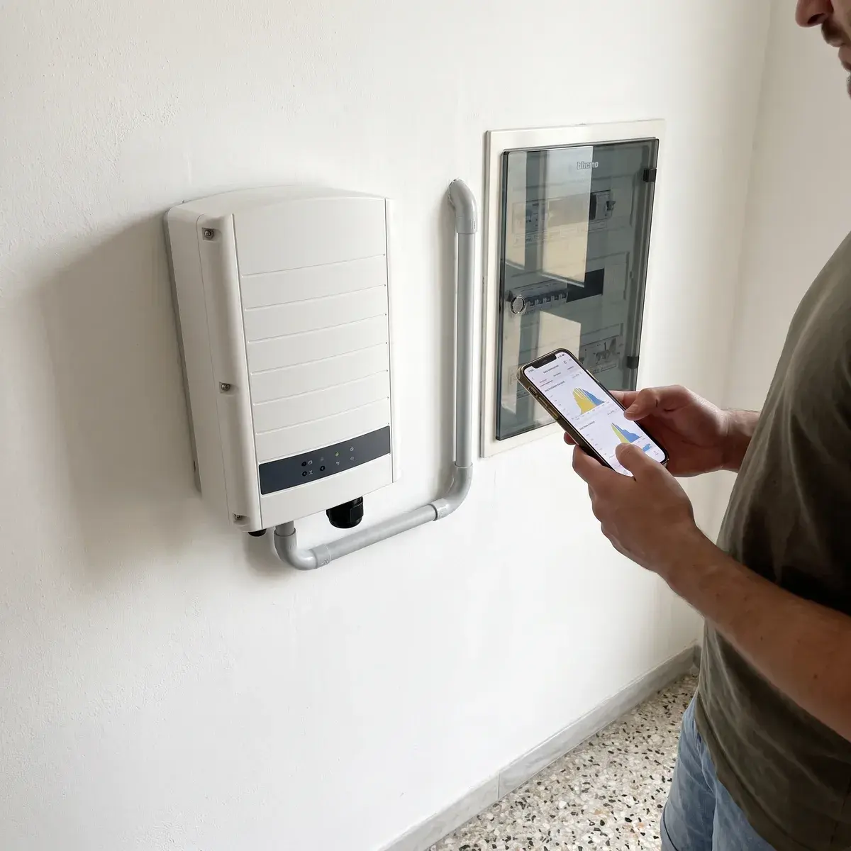 Proprietario che legge la produzione sul telefono accanto a un inverter SolarEdge Home Wave e al quadro elettrico incassato.