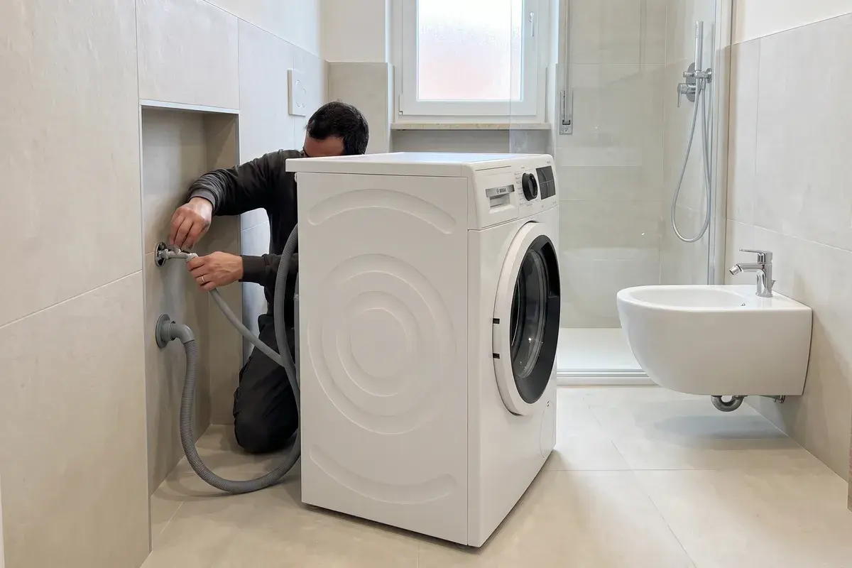Installatore che collega il tubo di carico di una lavatrice Bosch Serie 6 WGG244Z8IT al rubinetto nel bagno ristrutturato di un appartamento.
