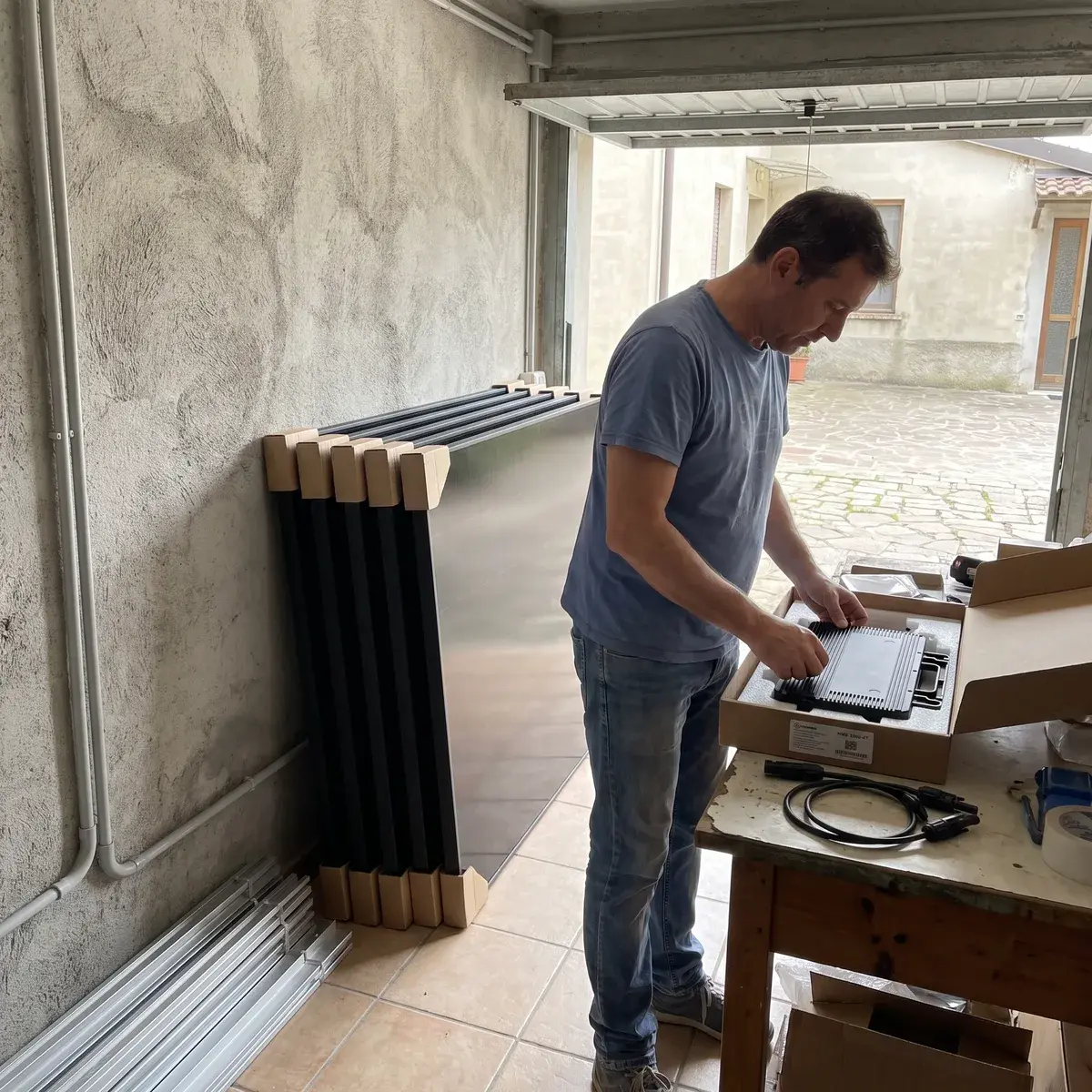 Privato che apre la scatola di un microinverter Hoymiles HMS-2000-4T in garage, con quattro moduli AIKO Neostar appoggiati al muro.