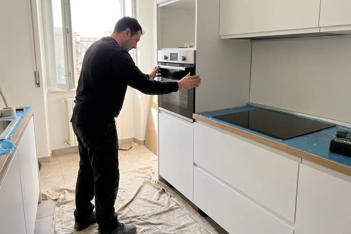 Montatore che inserisce un forno da incasso Bosch Serie 4 HBA514BS3 nella colonna di una cucina nuova, con il piano a induzione Bosch già montato.