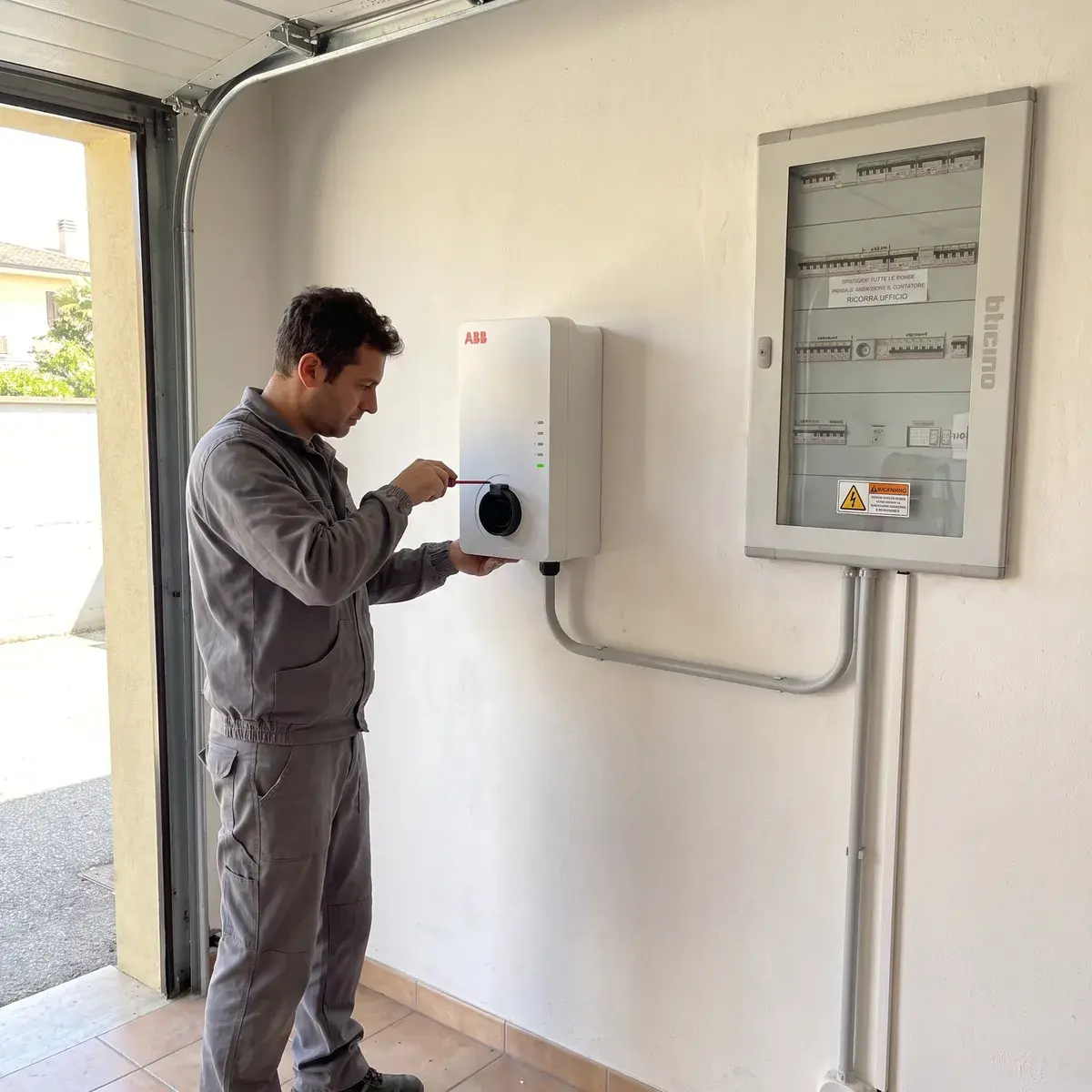 Elettricista che fissa una wallbox ABB Terra AC alla parete del garage, con il tubo in PVC grigio che arriva dal quadro BTicino.