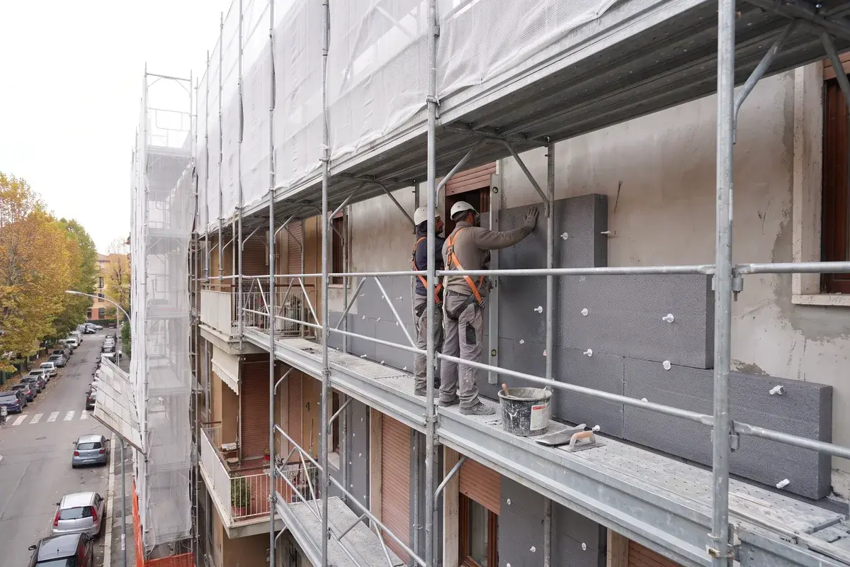 Operai su un ponteggio fissano con i tasselli pannelli isolanti in EPS grafitato sulla facciata di un condominio degli anni Settanta.
