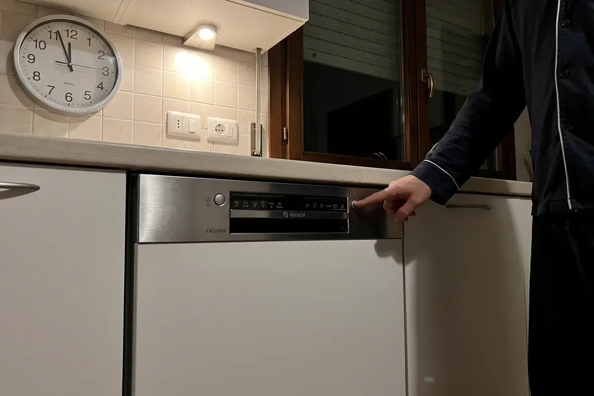 Persona in pigiama che avvia di sera una lavastoviglie Bosch Serie 4 SMI4HBS12E in una cucina italiana, con l’orologio a muro poco dopo le 23.