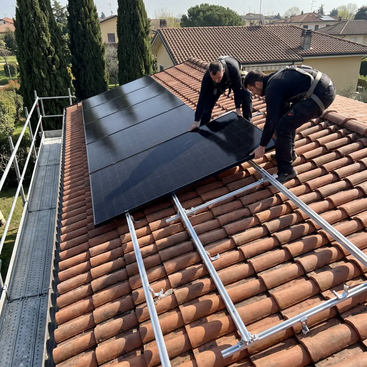 Due installatori posano un modulo Trina Vertex S+ full black sulle guide K2 di un tetto in coppi, con il ponteggio in gronda.