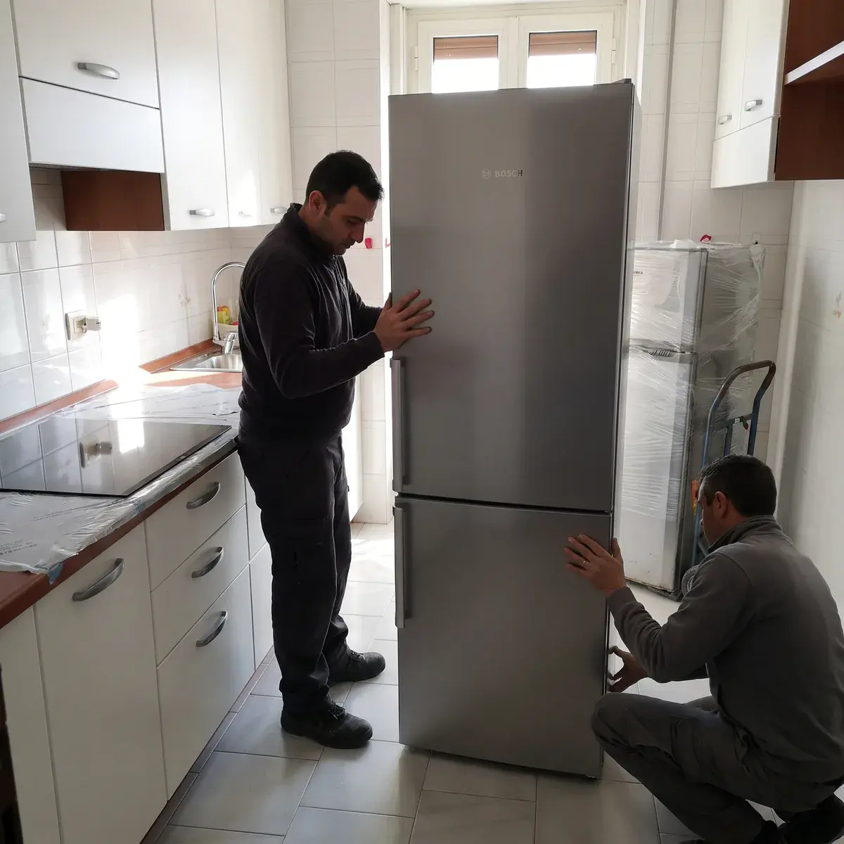 Due tecnici spingono un frigorifero combinato Bosch Serie 4 KGN39VLCT nel vano di una cucina appena montata, con il vecchio frigo imballato sul carrello.