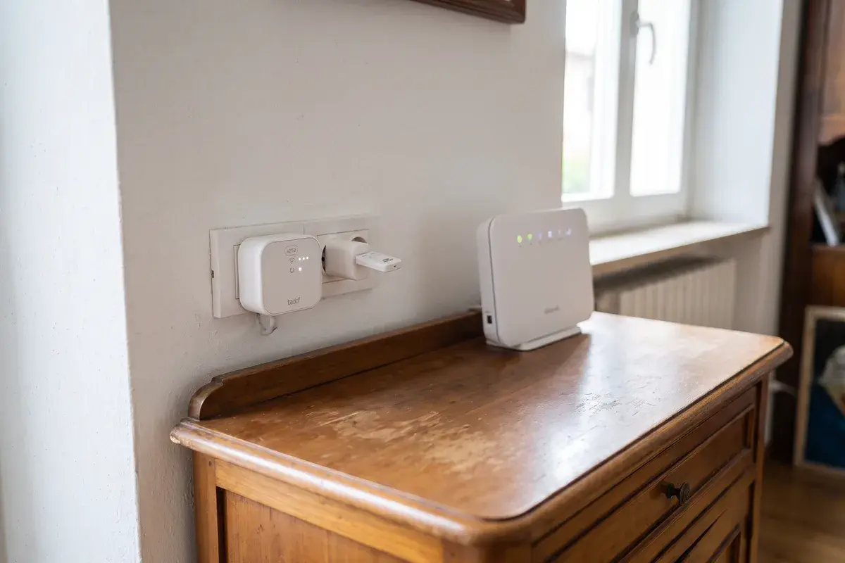 Un tado Bridge X inserito in una presa BTicino Living Now in corridoio e, nella presa accanto, uno Shelly BLU Gateway Gen3 su un alimentatore USB, con il router di casa sul mobile.