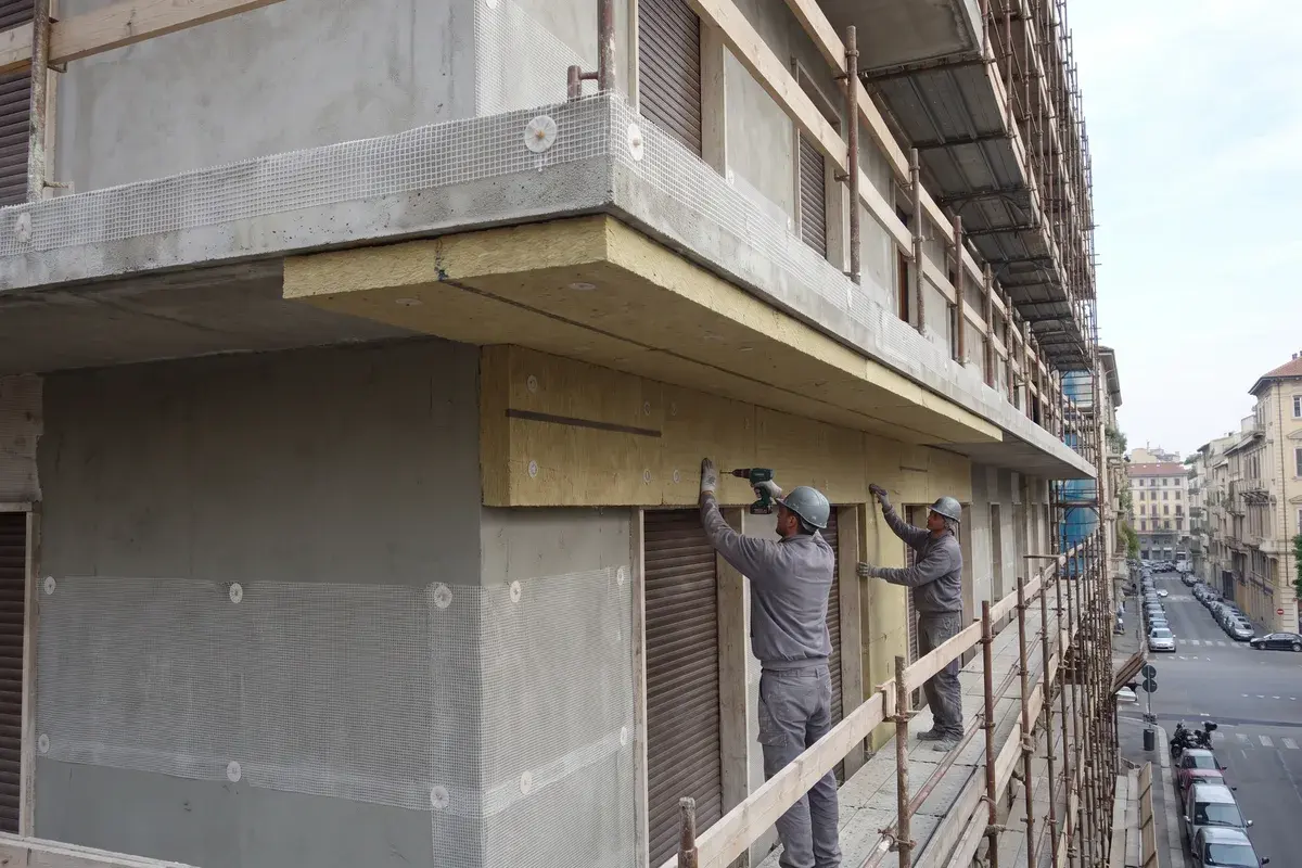 Due operai sul ponteggio di un condominio fissano con i tasselli pannelli in lana di roccia Rockwool Frontrock Max Plus attorno alla soletta di un balcone.