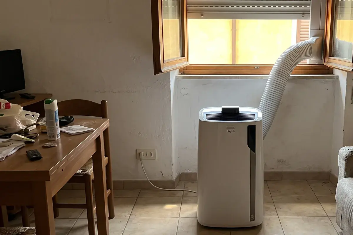 Condizionatore portatile De'Longhi Pinguino PAC EL98 sul pavimento di un soggiorno, con il tubo di scarico fissato al kit per la finestra socchiusa.