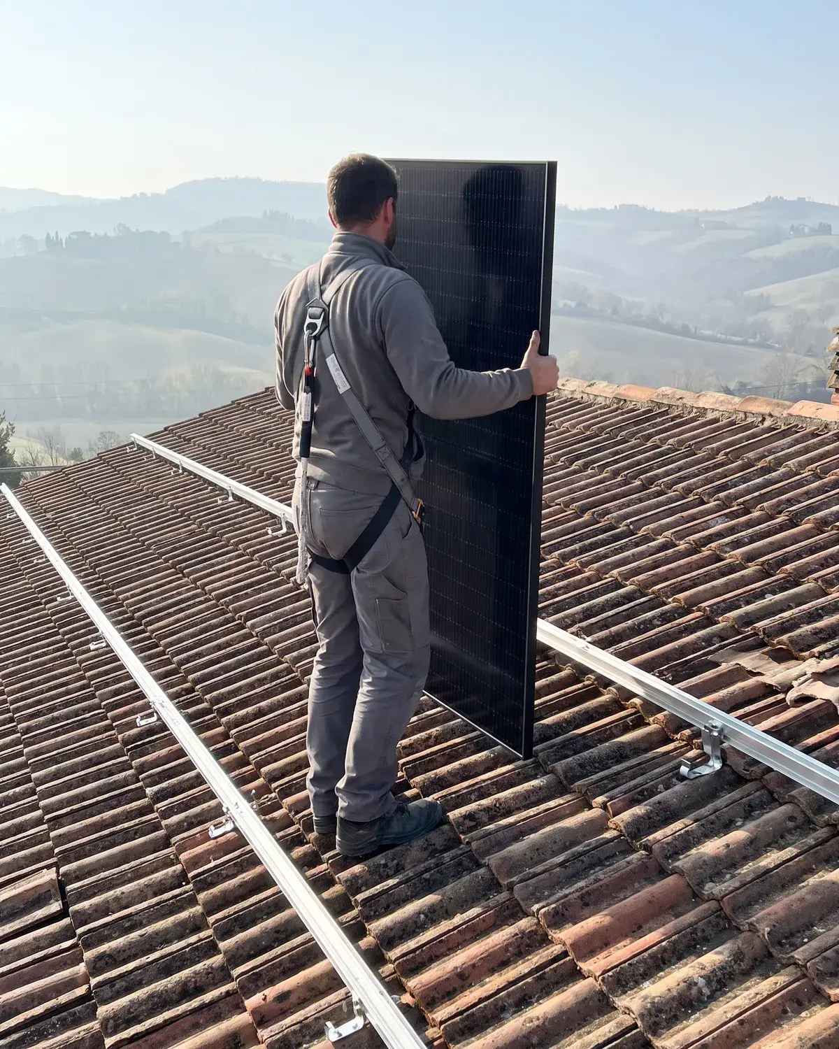 Installatore con imbracatura porta un modulo Trina Vertex S+ sul tetto, sopra le guide di montaggio