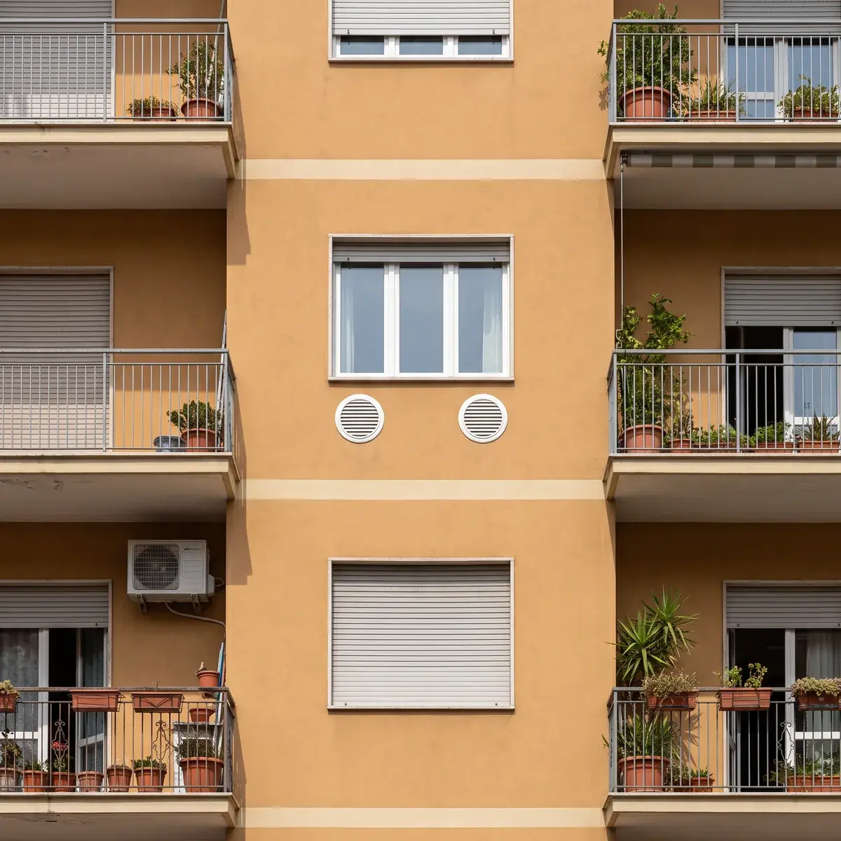 Facciata ocra di un condominio con le due griglie tonde di un climatizzatore senza unità esterna Olimpia Splendid Unico Pro sotto una finestra e, più in basso, l'unità esterna di uno split su un balcone vicino.