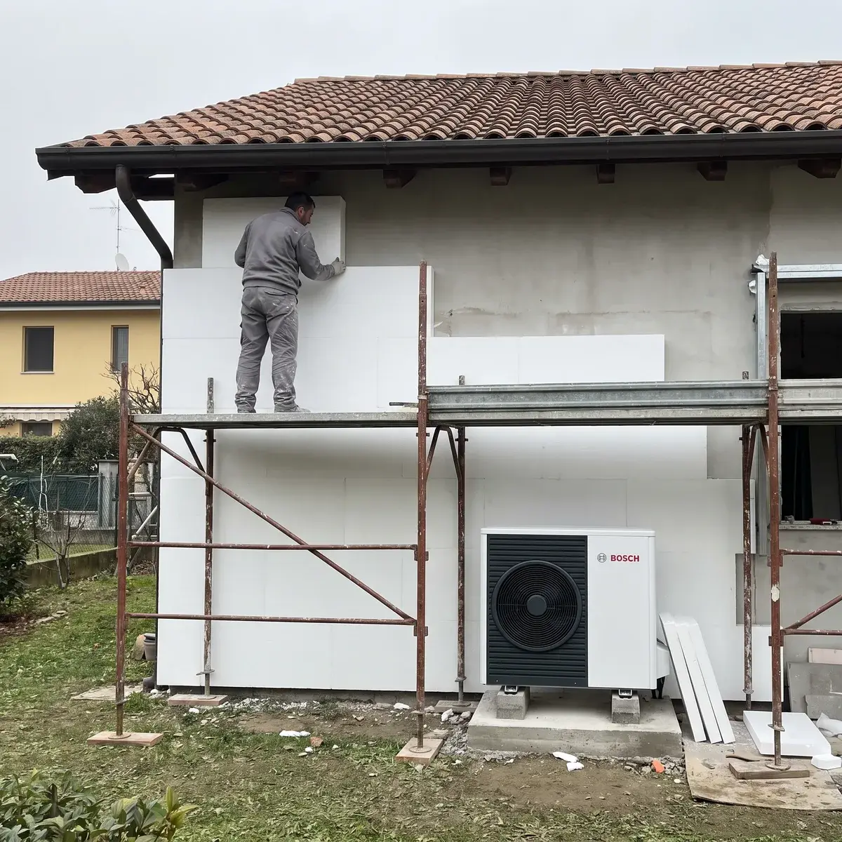 Villetta in fase di isolamento a cappotto, con il ponteggio sulla facciata e un'unità esterna Bosch Compress 5800i AW già installata.